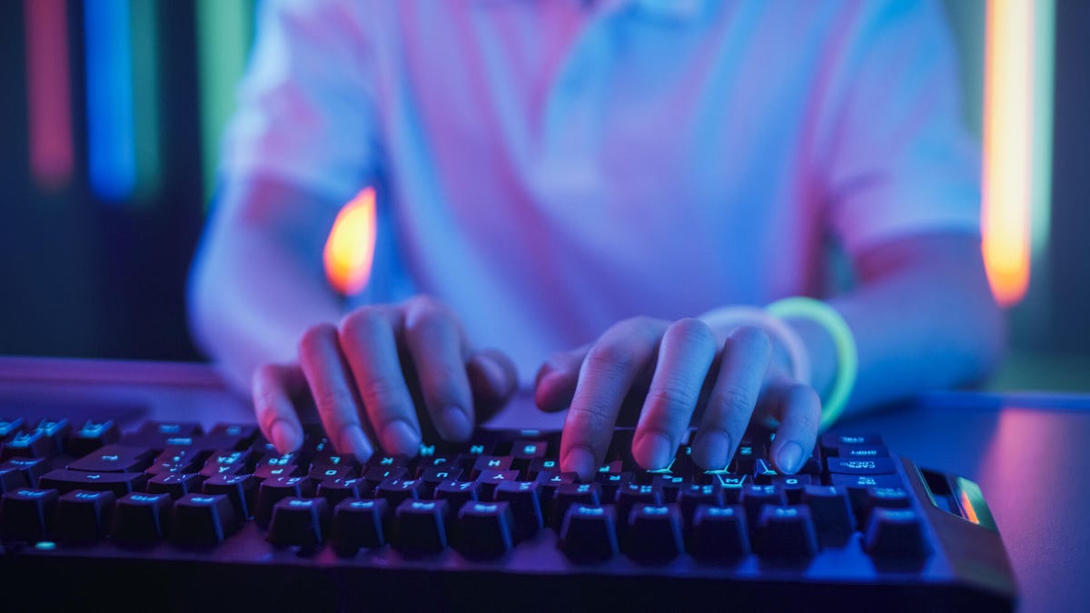 A photo of someone's hands typing on a keyboard, with neon backlighting gettyimages-1010650348