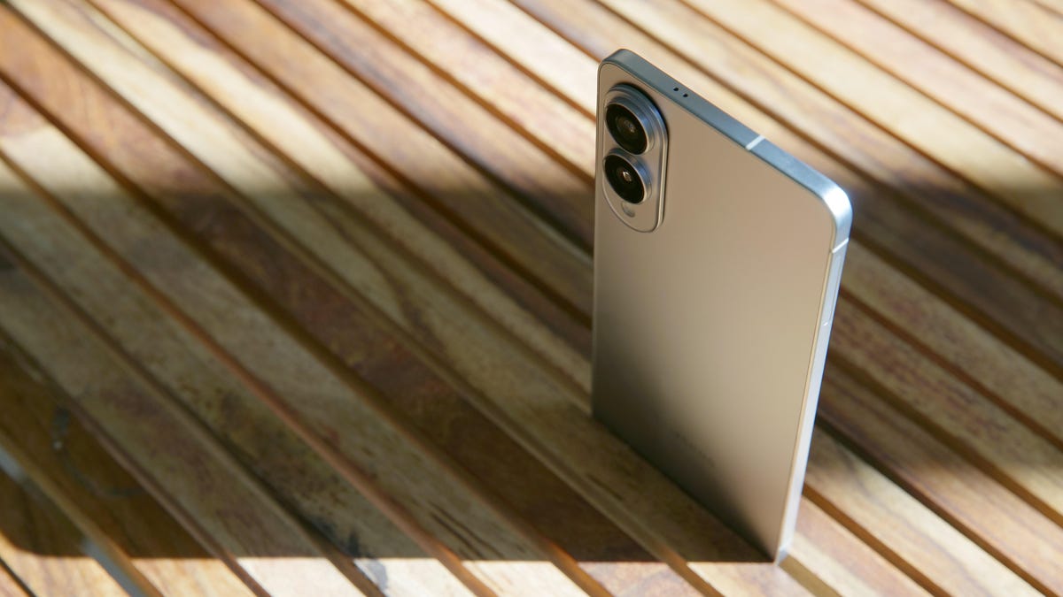 A thin phone standing upright by being slid between the slats of a wooden table.