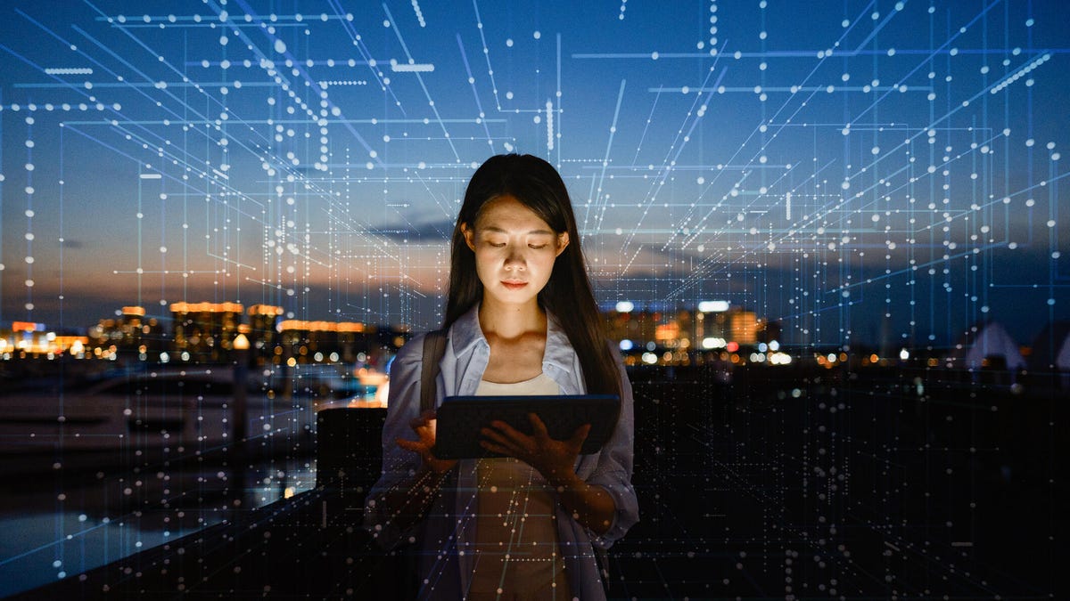 Asian woman using artificial intelligence on a tablet standing in front of a city scape.