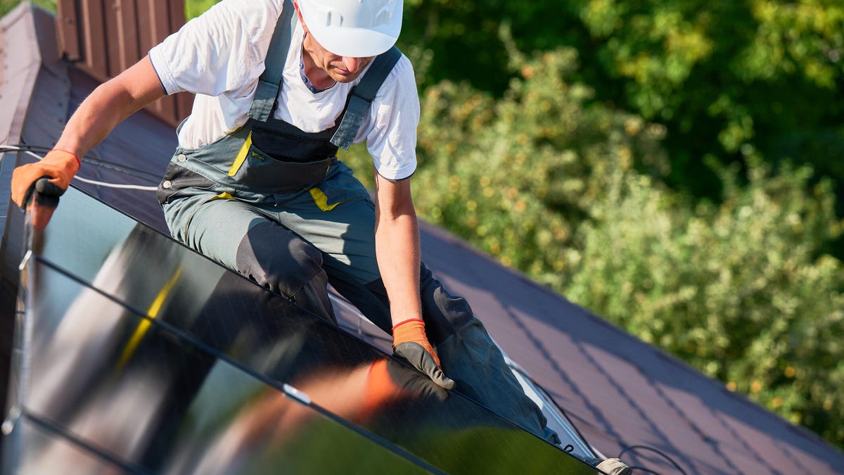 A solar panel installer puts a panel on a rooftop.
