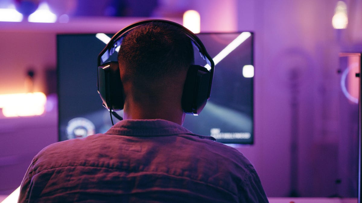A person plays video games with headphones on and a purple glare