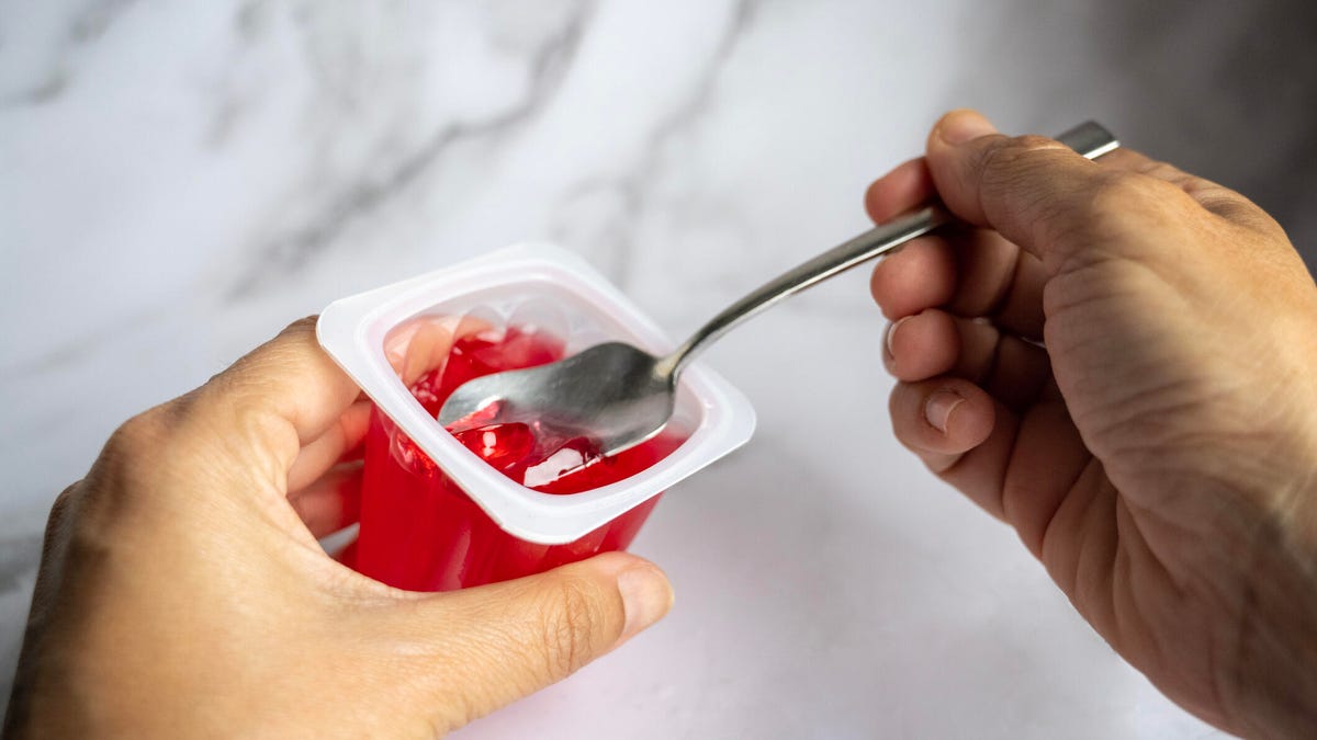 A person's hands eating out of a cup with red Jell-O.
