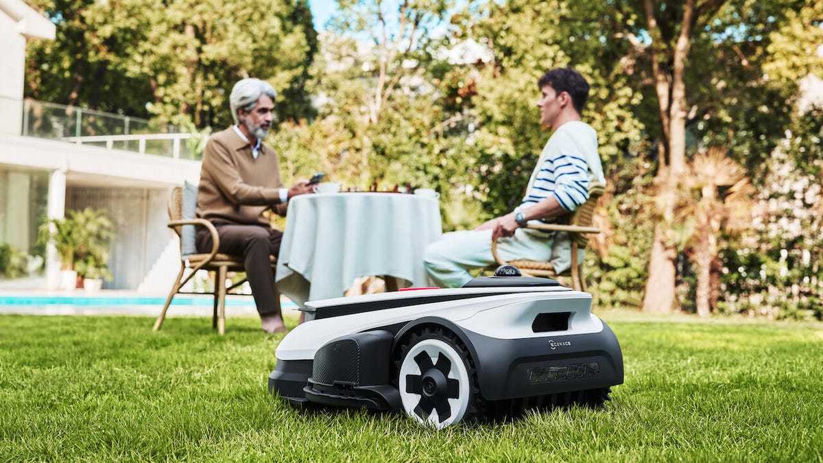 Robot lawnmower on a lawn with people in the background.