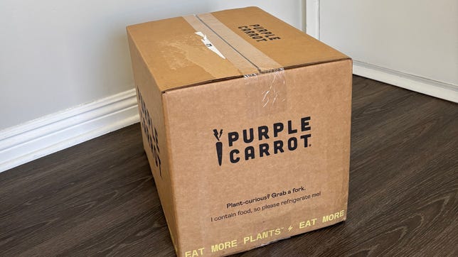 The Purple Carrot box on a grey wood floor.