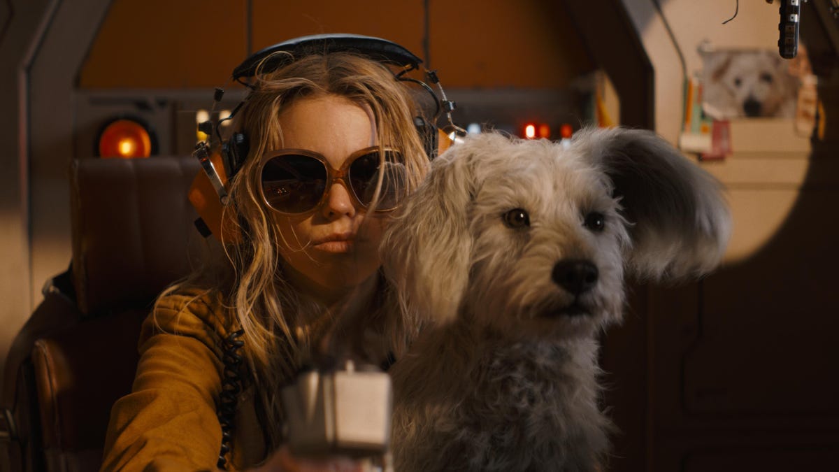 supergirl wears headphones while sitting with Krypto on her lap