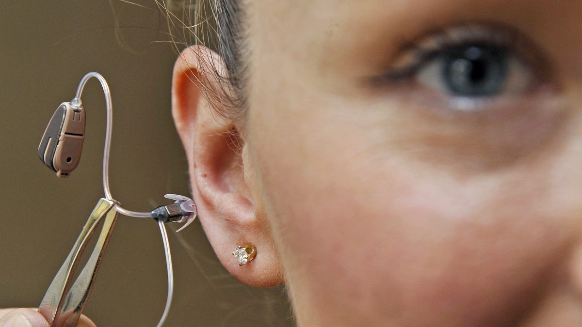 Close-up of woman's ear as she inserts a hearing device