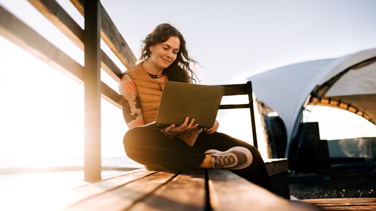 Three friends, with the sunset as their backdrop, taking selfies with their smartphones.