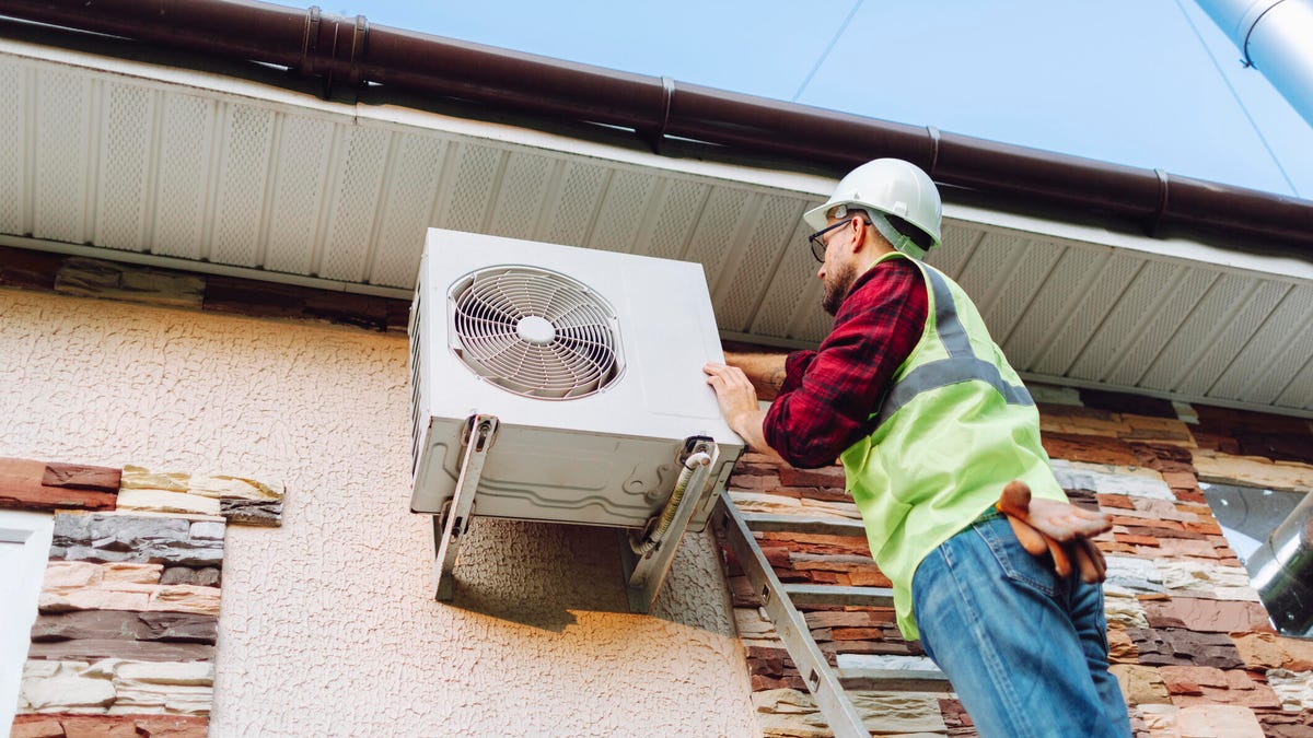 A technician installing a heat pump on the outside of a home.