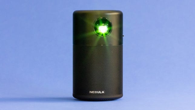 The Anker Nebula Capsule shines greenish star-shaped light while sitting on a light blue background.