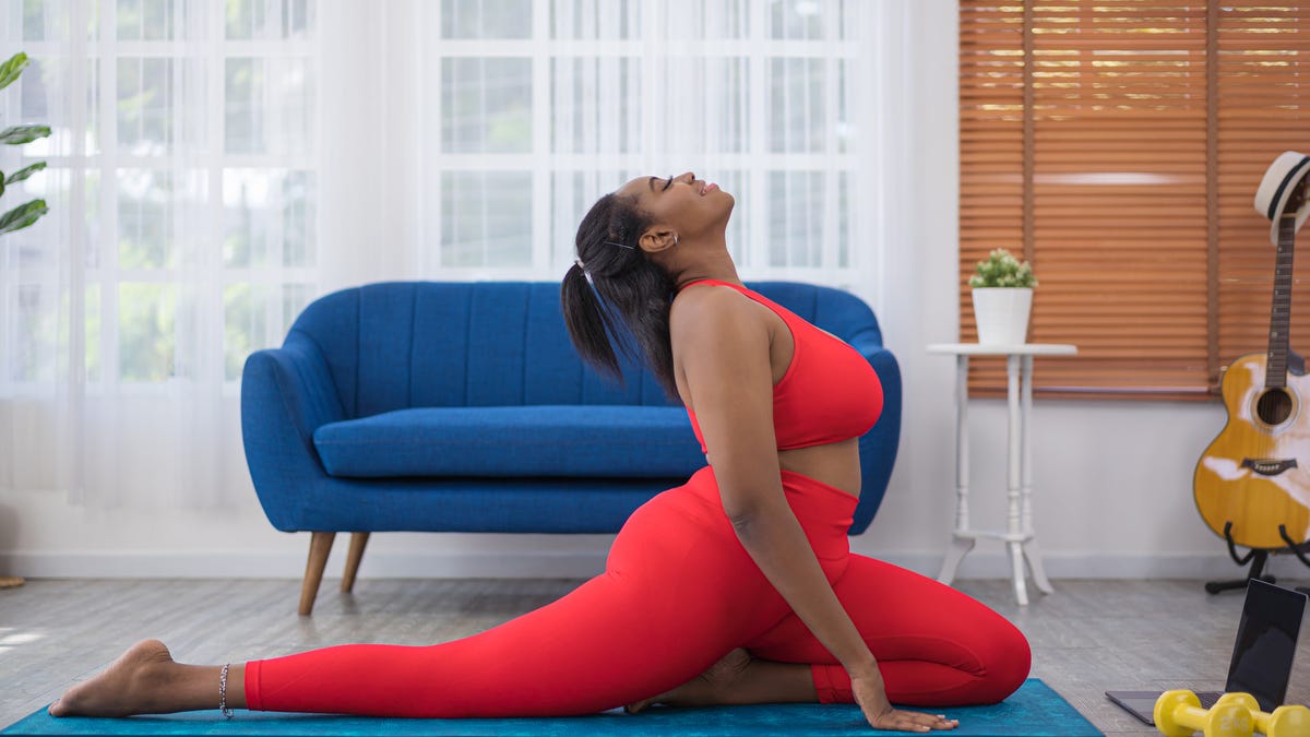 A woman in neon gym clothes performs a yoga pose in a lounge room.
