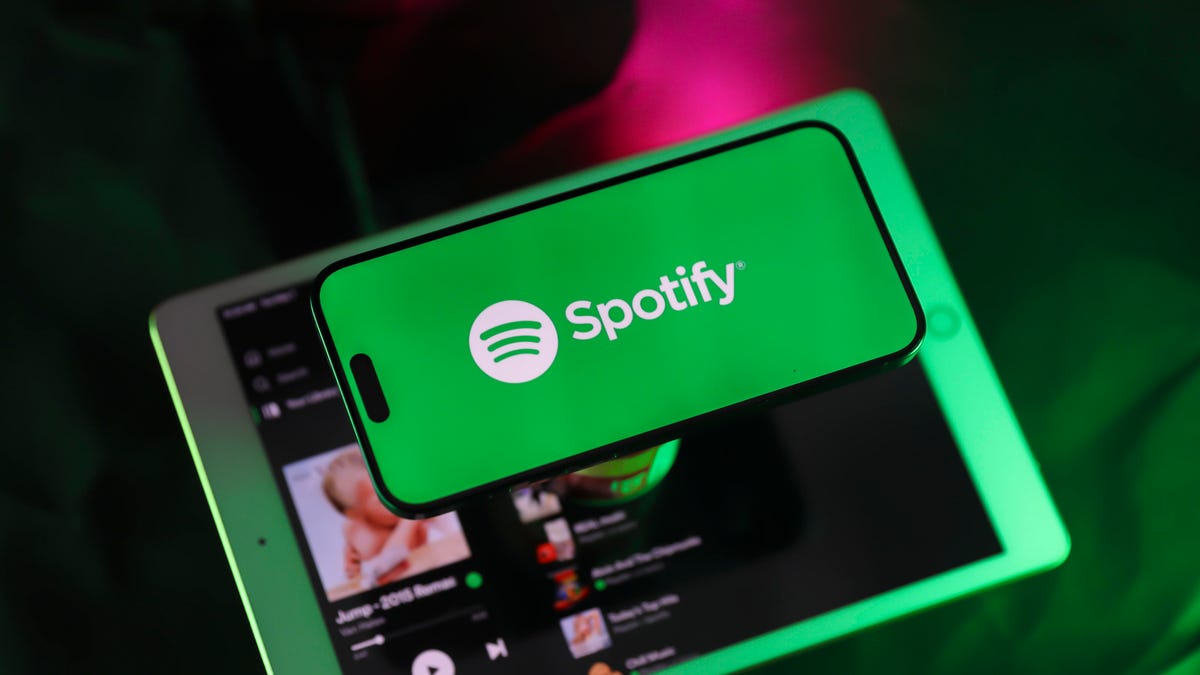 A phone lies on top of a tablet. On the phone screen is Spotify's logo. On the tablet, the Spotify app is open.