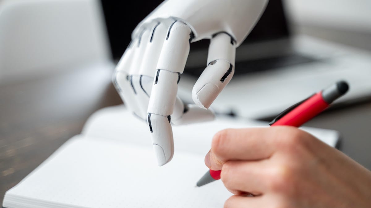 A white robot hand guides a human hand to help them write.
