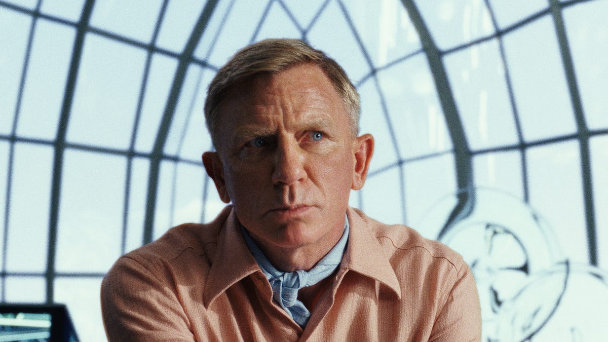 Daniel Craig looks thoughtful in a light pink shirt and natty blue neckerchief in murder mystery movie Glass Onion.