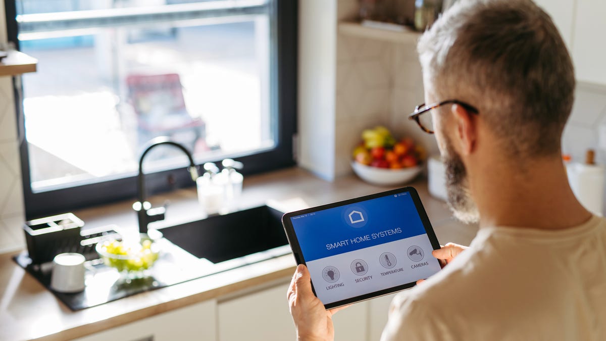 A man stands in a sunny kitchen looking at a smart tablet.