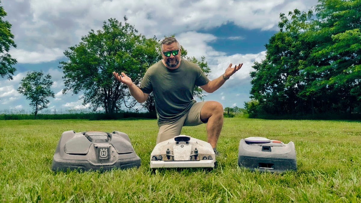man kneels in front of three robot mowers