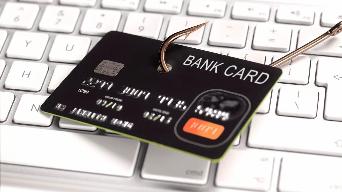 A bank card with a fishing hook through it in front of a computer keyboard.