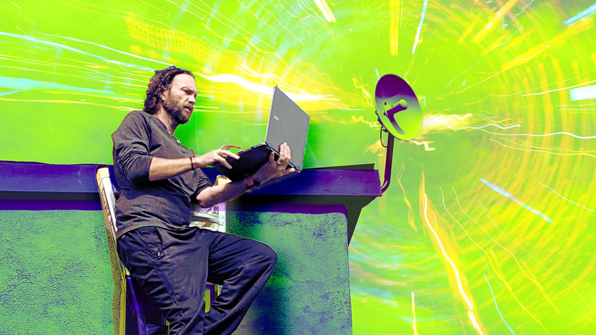 Eric Mack holding a laptop near the roof of his off-grid home.