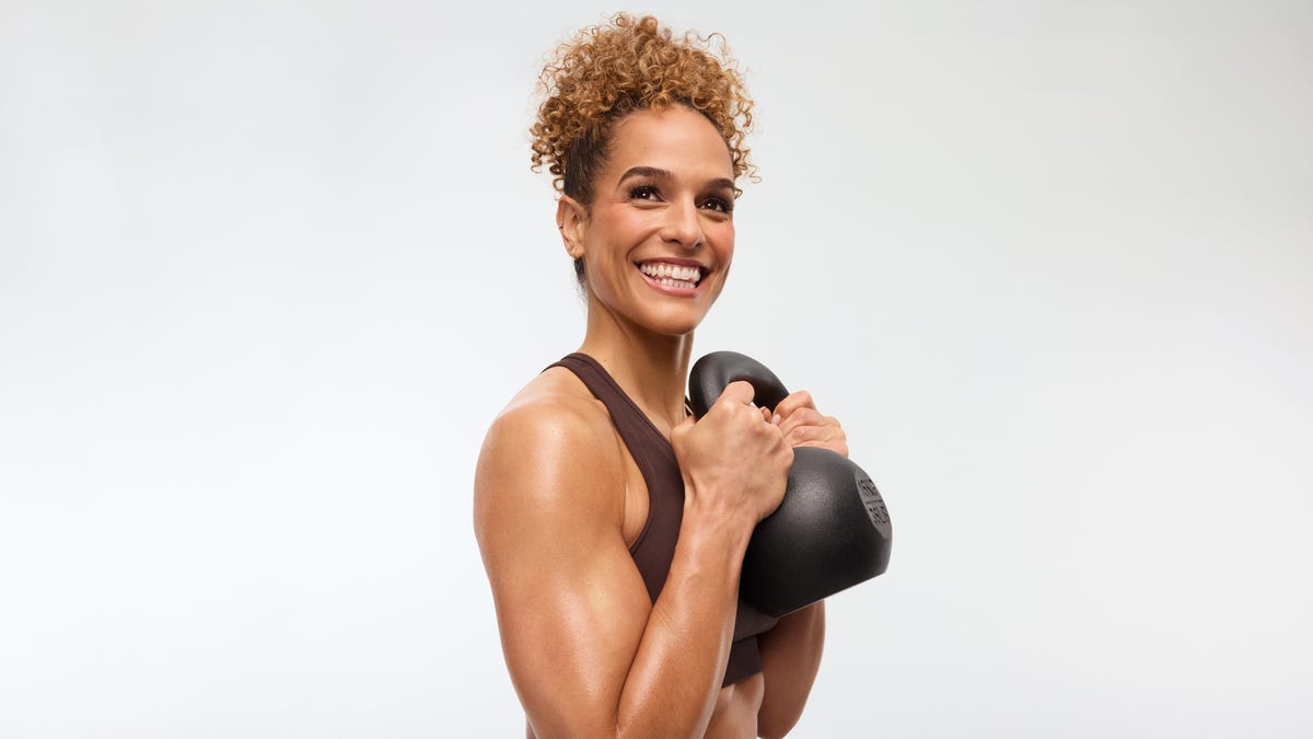 muscular woman in training top smiling holding a kettlebell