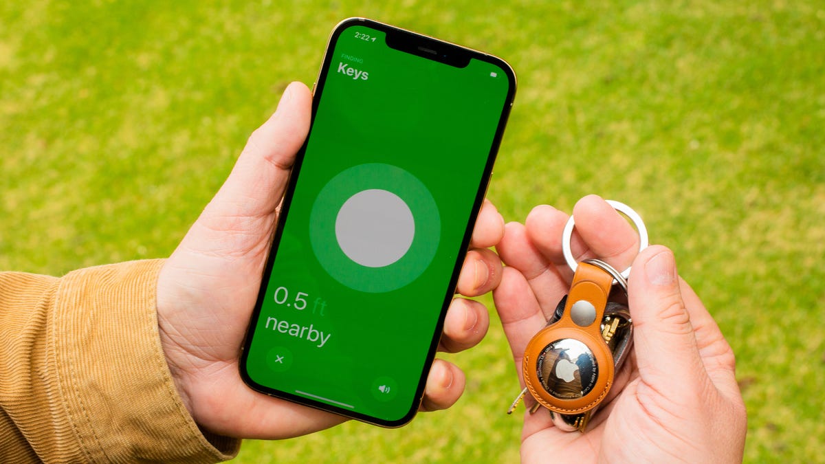 An Apple AirTag in one hand and an iPhone in the other showing the location of the AirTag