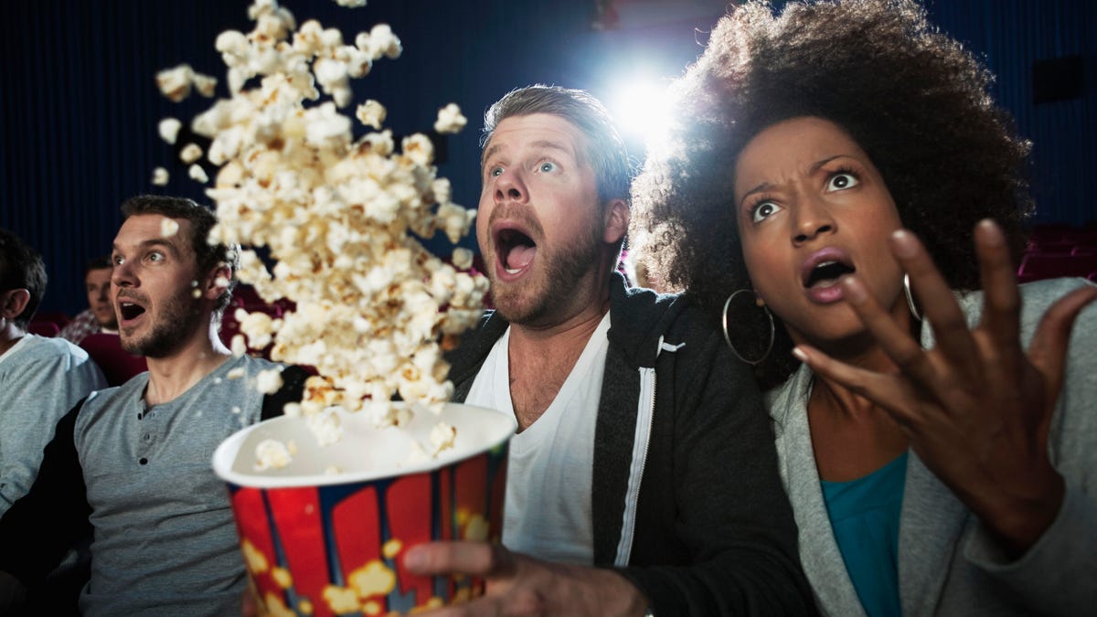 Three audience members at a movie gasp and throw popcorn in the air from shock
