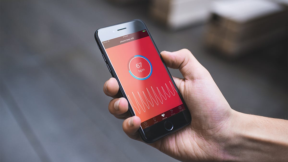 A hand holding a smartphone that is tracking heart rate.