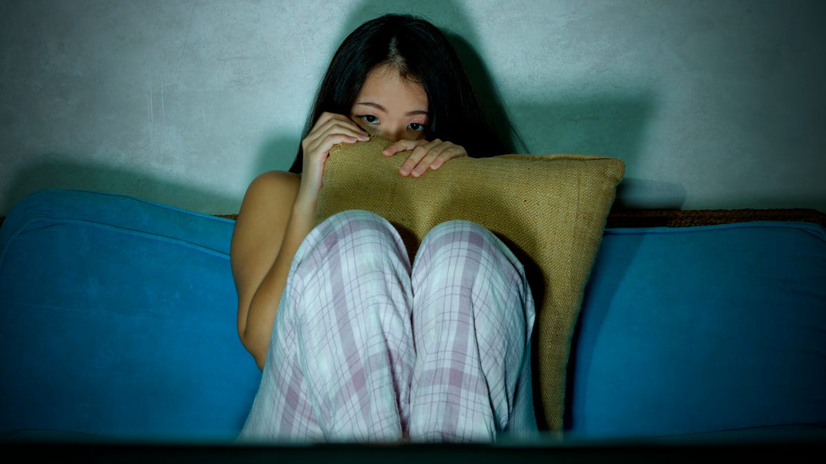 Woman hides behind a pillow while watching a movie.