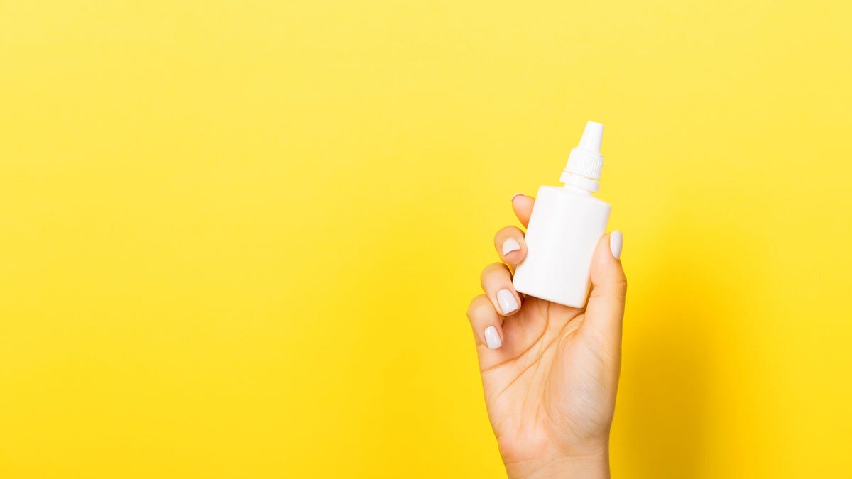 A hand holding a nasal vaccine spray against a yellow background