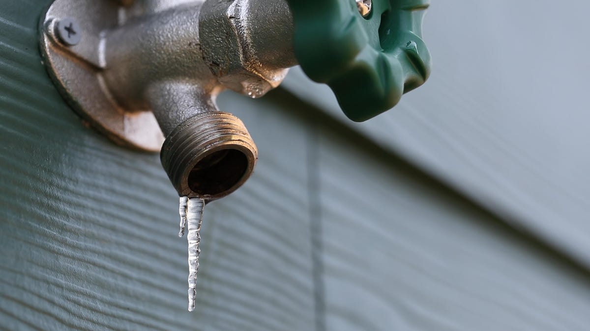 A small icicle on an outdoor faucet connected to siding.