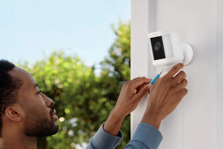 A man adjusts a Ring Spotlight Cam Plus installed on white exterior siding.