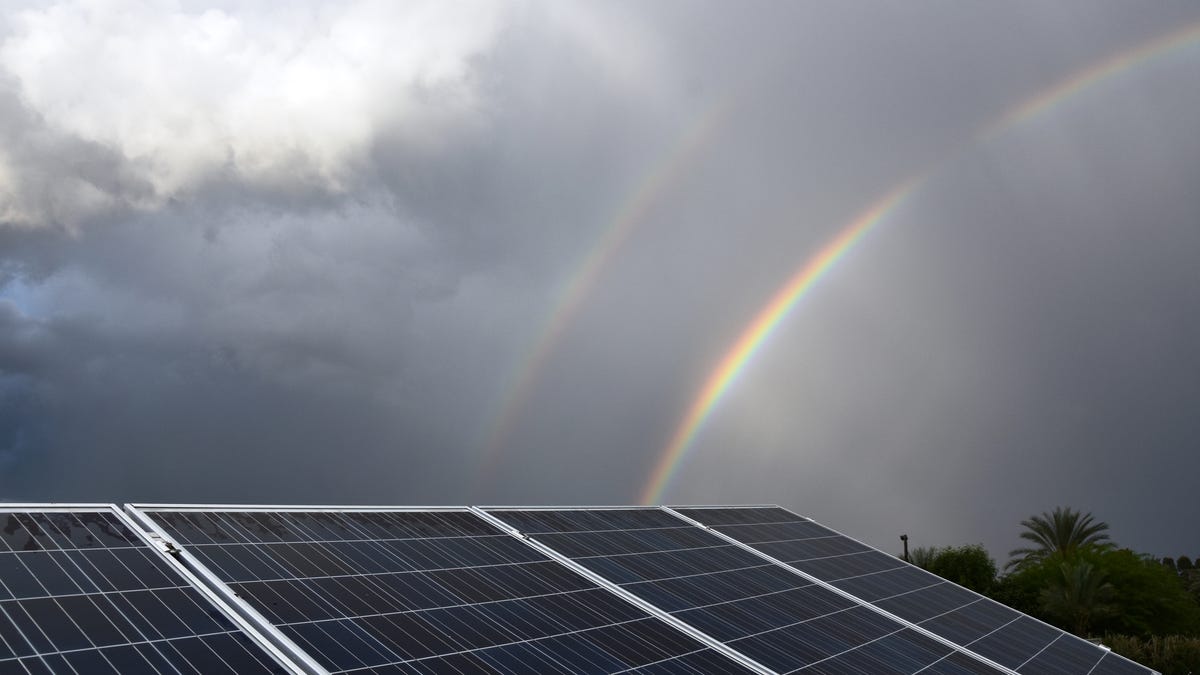 Solar panels with clouds and a rainbow in the background.