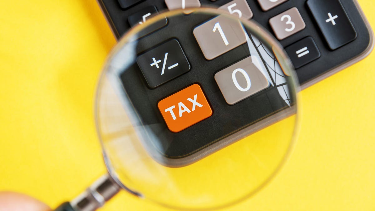 Magnifying glass on tax calculator against a yellow background