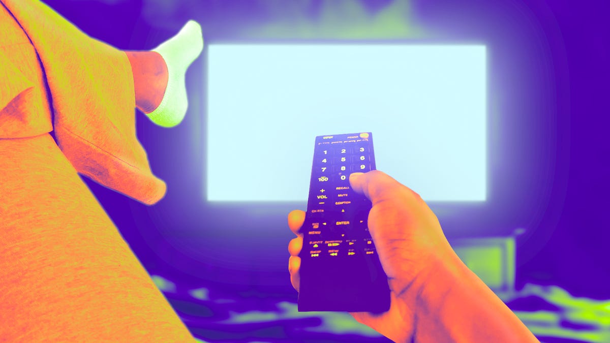 A person lounges on a couch with a remote and tv in the background.