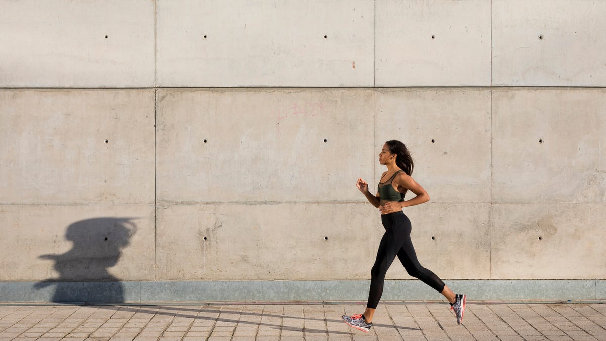 A woman running along a sidewalk and casting a long shadow on a concrete wall