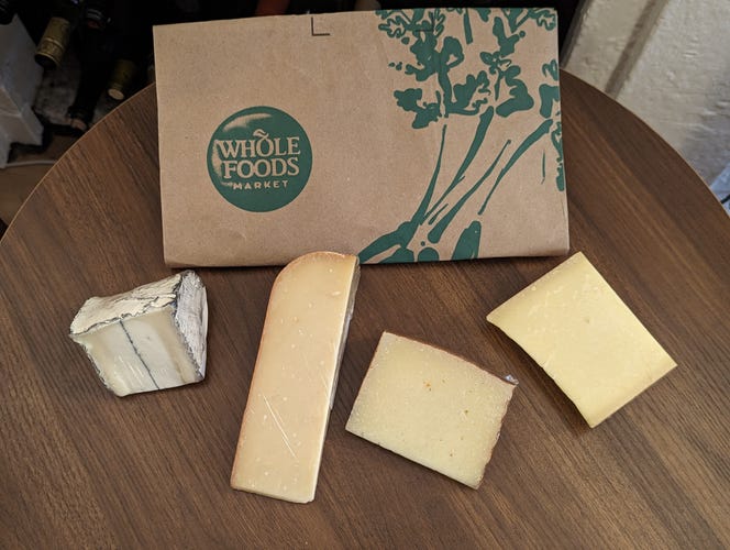 Four blocks of cheese in front of Whole Foods bag