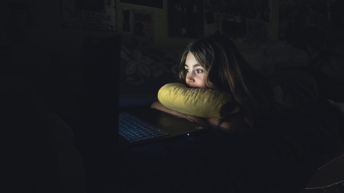 Young girl using laptop computer with face lit up by screen in bed at night.