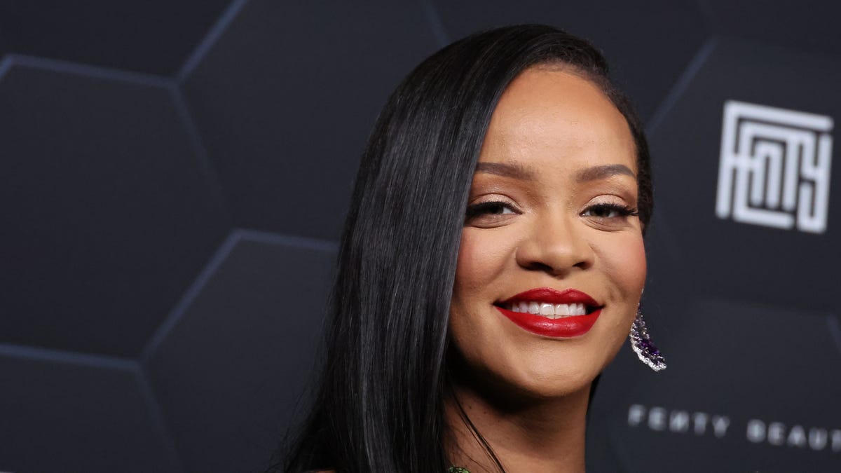 Rihanna smiles in close-up as she poses in front of a black backdrop