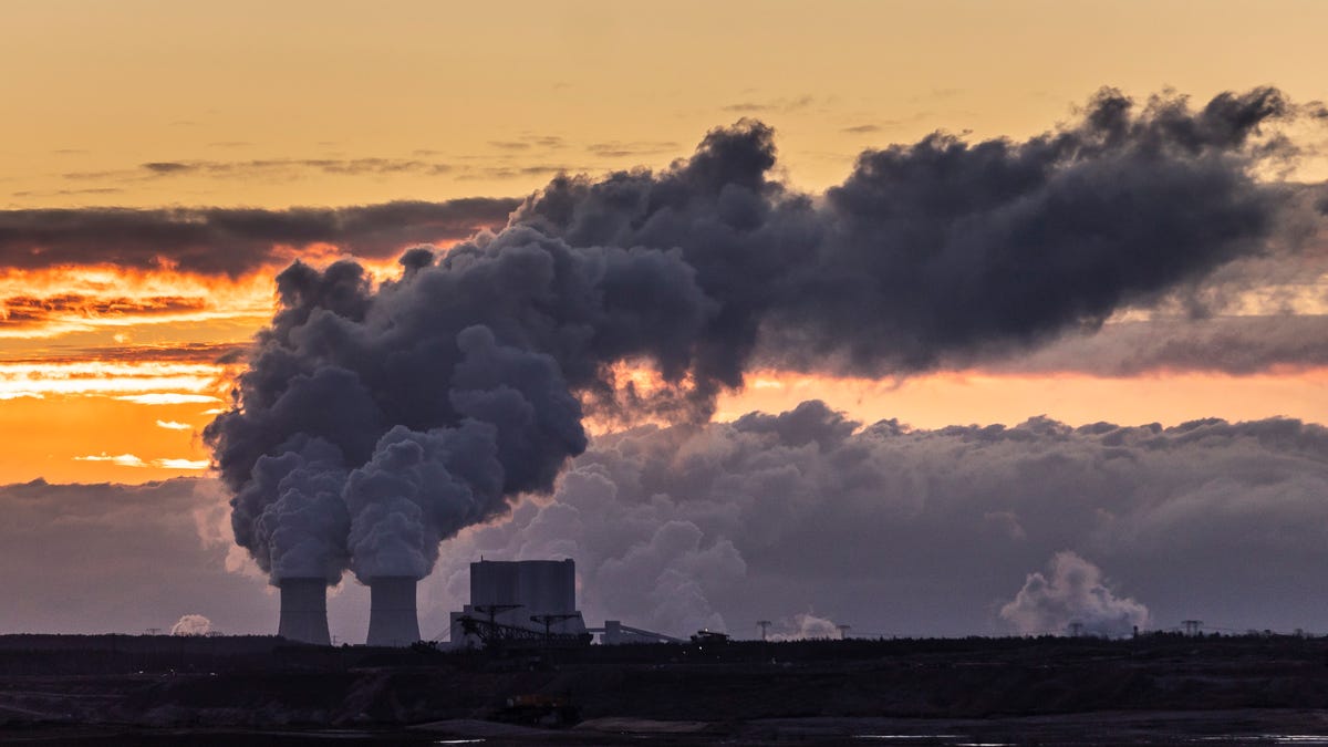 The sky is orange with sunset streaks, and in the foreground there's an industrial plant pumping thick clouds of smoke into the air. They're smoke clouds nearly indiscernible from natural clouds.