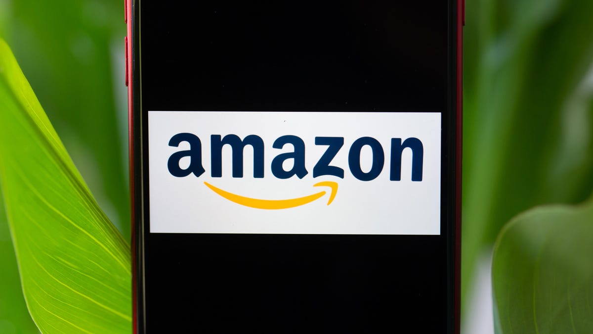 The Amazon smile logo on a phone screen, with green leaves behind the phone.