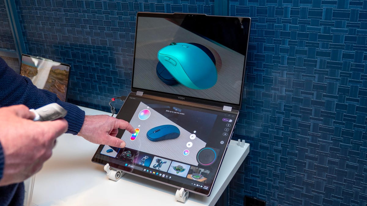 A man stands in front of the Yoga Book 3D concept using the clip-on tools to alter the picture on the dual-screen computer. The bottom screen shows a 2D image of a mouse, while the top screen shows a 3D rendering of the same image.