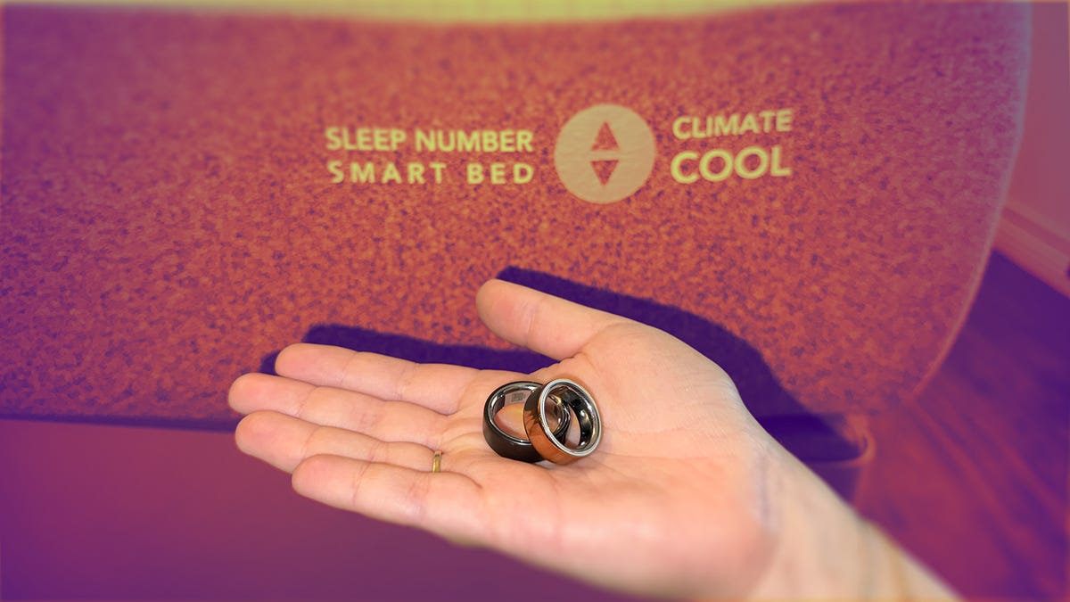 A hand holds two Oura Rings near the Sleep Number bed logo