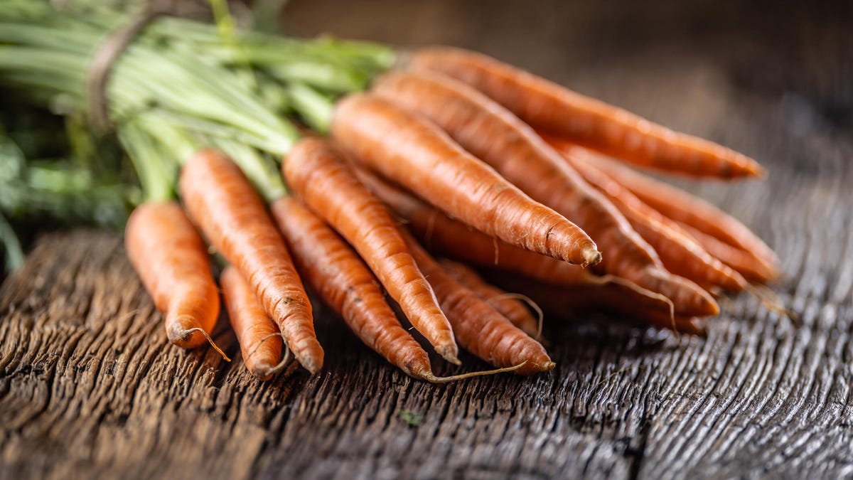 Fresh carrots laid loosely on an old table.