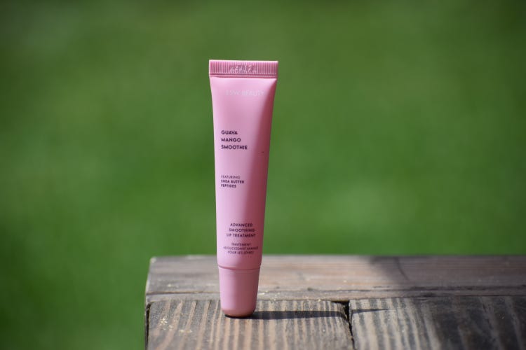 ESW Beauty Guava Mango Lip Treatment on a wood surface in front of a blurred green background.