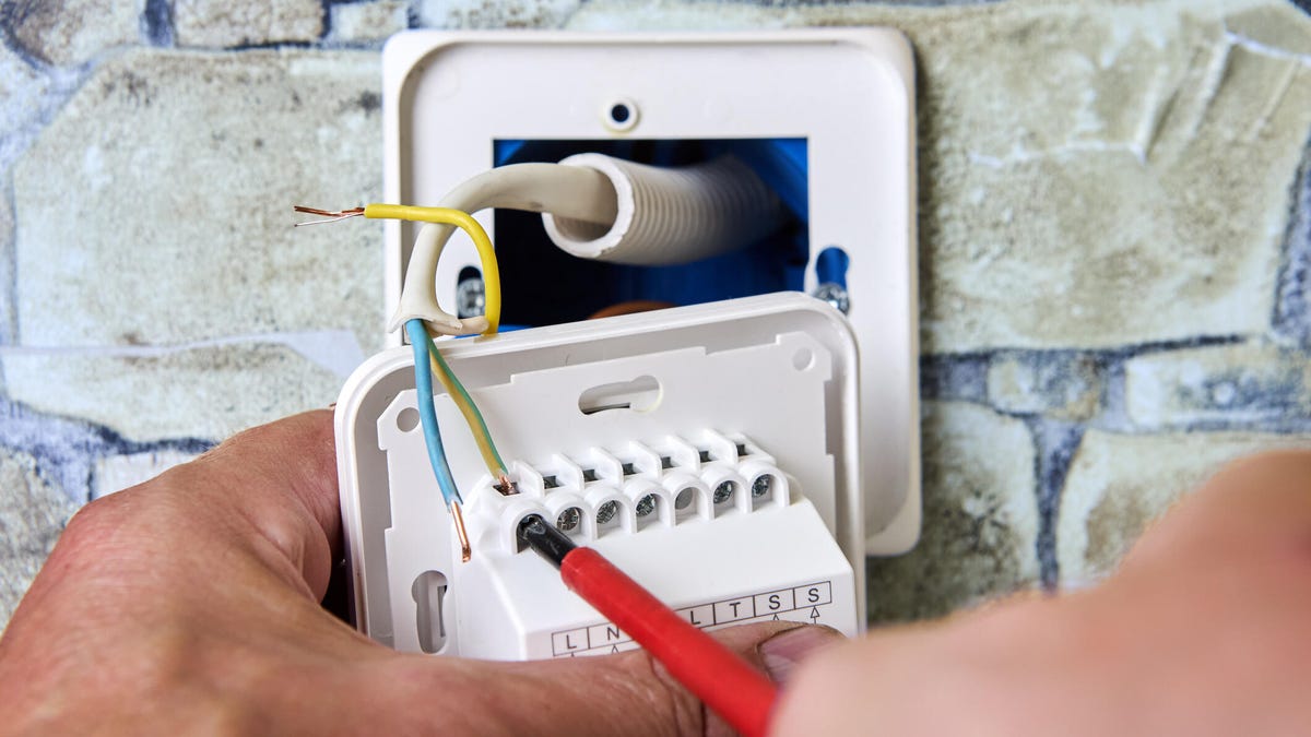 Hands unwiring a thermostat model on a stone wall.