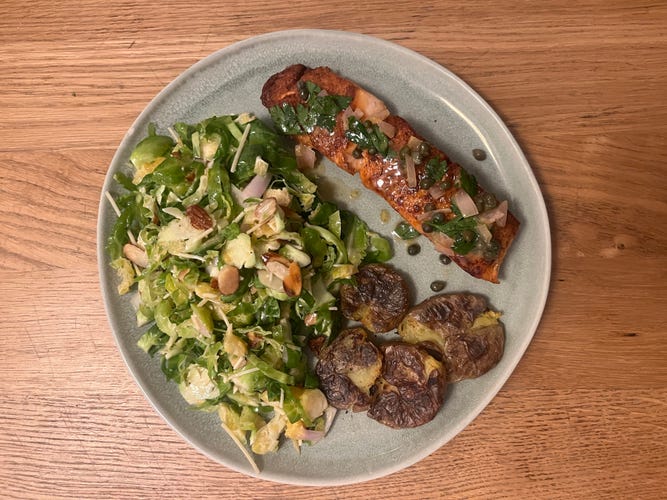 a plate with salmon, salad and smashed potatoes on it.