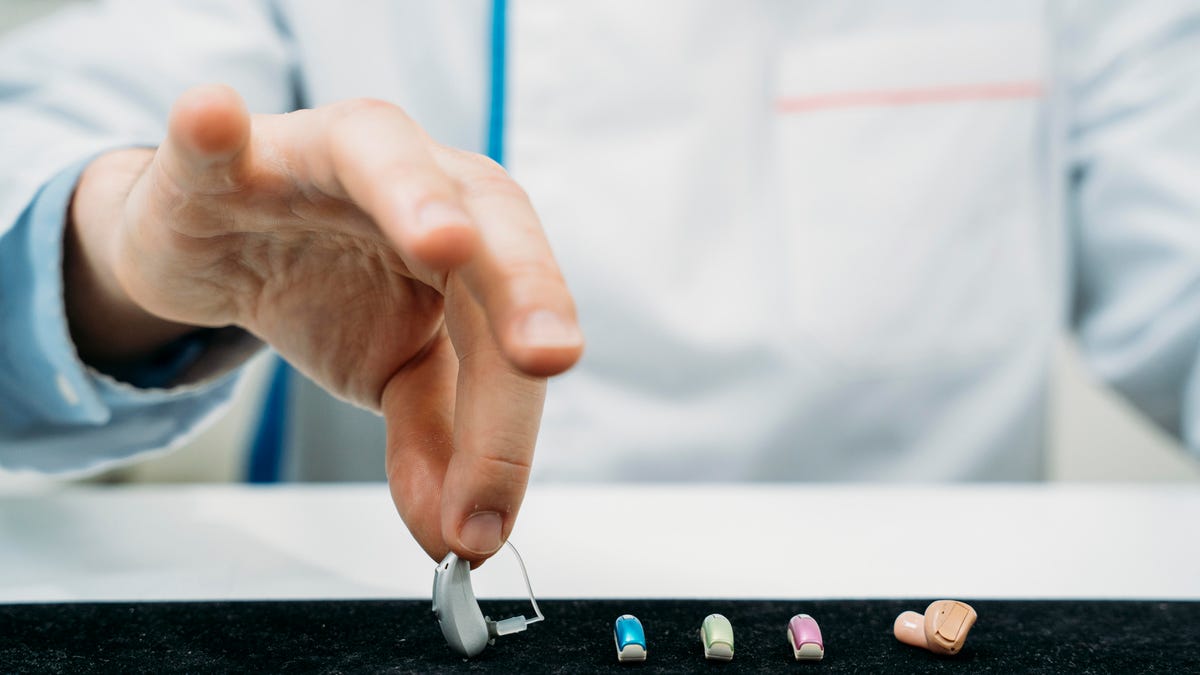 A hand selecting a hearing aid among a few colorful choices