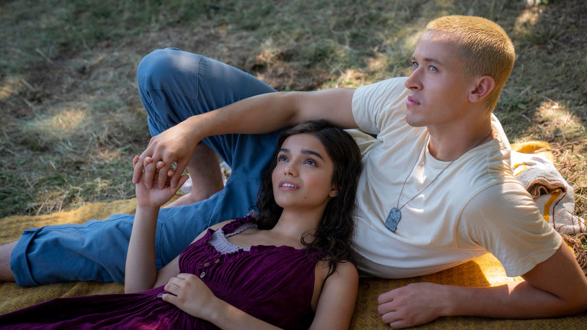 Rachel Zegler and Tom Blyth relax together on a blanket outside and hold hands.