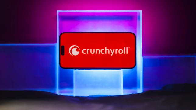 A cellphone on a stand has the Crunchyroll app pulled up on its screen.