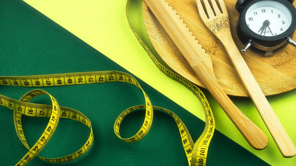 A tape measure, alarm clock and wooden knife and fork against a neon green background
