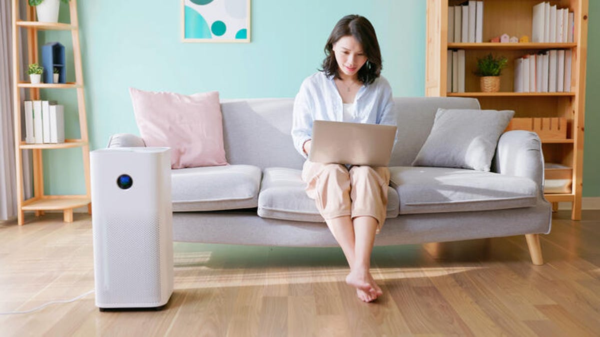 Woman sitting on her couch with an air purifier next to her.