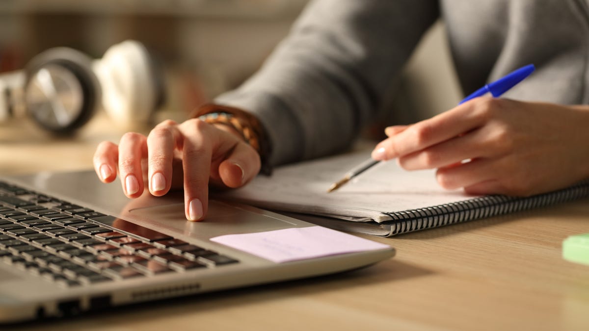 Close up of a woman's hands comparing laptop content and her notebook.